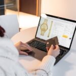 Buy Now, Pay Later: The Financial Trap Hiding in Plain Sight Person holding a credit card while shopping online for a watch on a laptop