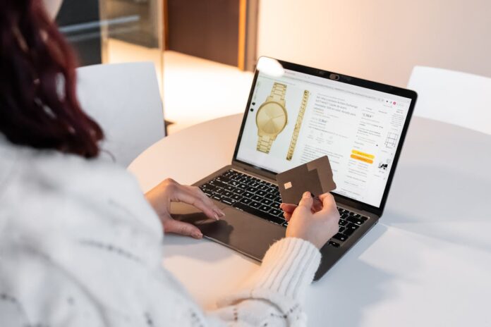 Person holding a credit card while shopping online for a watch on a laptop