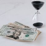 Why Low-Cost Index Funds Beat Wall Street’s Old Playbook A stack of dollar bills next to an hourglass filled with black sand