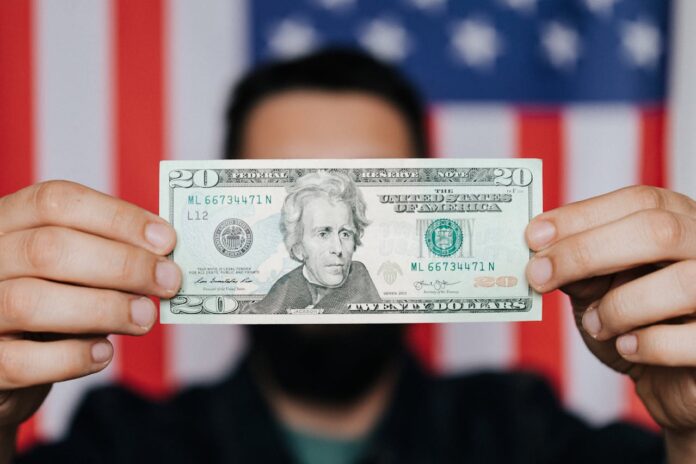 Person holding a twenty dollar bill in front of an American flag