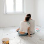 How Budget Home Renovations Are Reshaping American Living in 2025 A couple sitting on the floor of a freshly painted room, surrounded by painting supplies