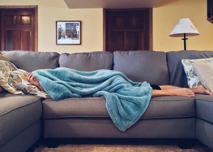 A person lying on a sofa covered with a blue blanket in a cozy living room
