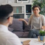 How Stress Management Became a Public Health Priority A woman expressing herself during a therapy session with a male therapist in a modern setting