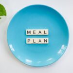 Why Meal Planning Is Replacing Diets for Healthier, Cheaper Living Blue plate with scrabble tiles spelling 'MEAL PLAN' and a green plant